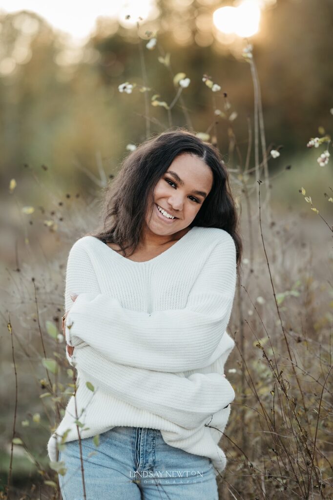 senior girl wearing a sweater in a grass field during her senior photography experience