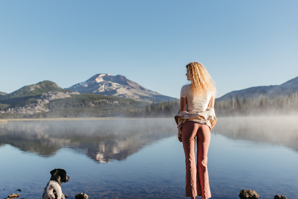 senior girl standing in front of Sparks Lake with her dog at one of my favorite senior photo locations