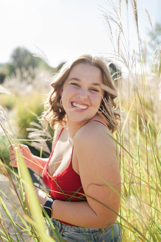 Senior girl smiling in the middle of grass for her senior photos