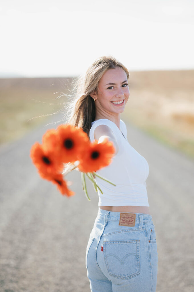 high school senior girl holding orange flowers on a gravel road