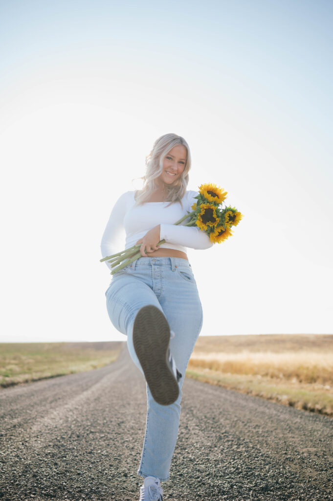 high school senior girl holding sunflowers on a gravel road