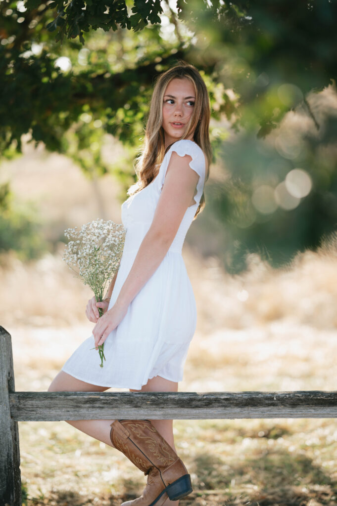 high school senior in a white dress holding baby's breath by an oak tree.