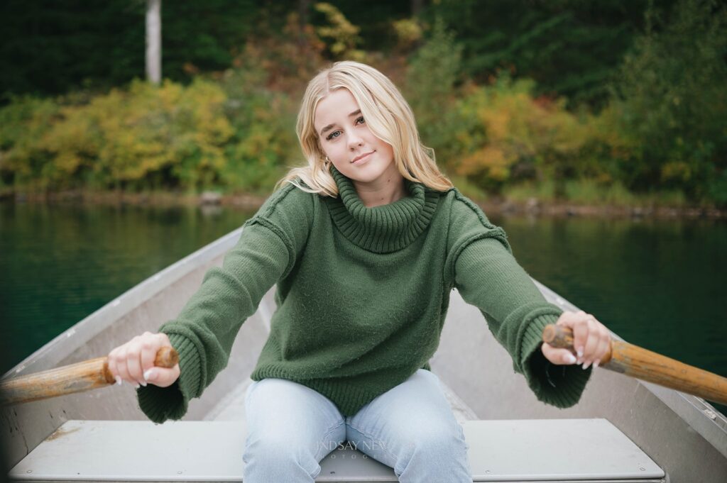 fall senior session of a high school senior in a green sweater rowing a boat on Clear Lake in Oregon. 