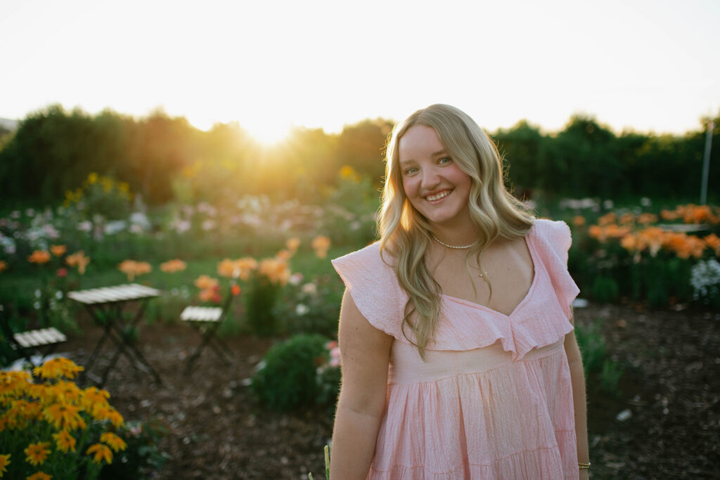 Dreamy golden hour portrait of a high school senior surrounded by flowers and glowing evening light.