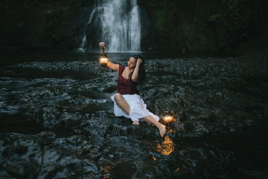 high school senior sitting in front of a waterfall with lanterns at Silver Falls State Park